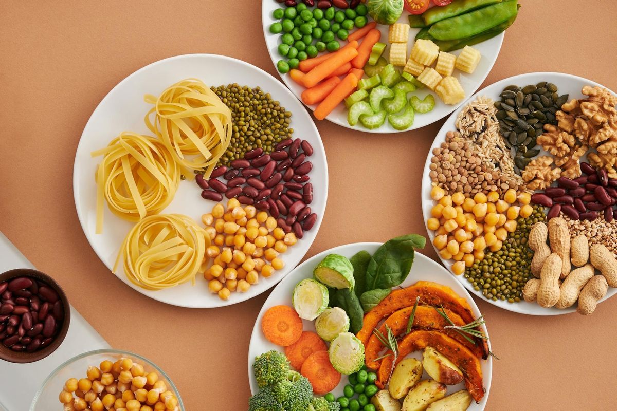A vibrant mix of legumes, vegetables, nuts, and pasta arranged on white plates.