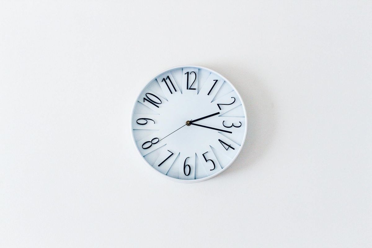 A simple minimalist wall clock against a white wall, suggesting time-based eating windows.