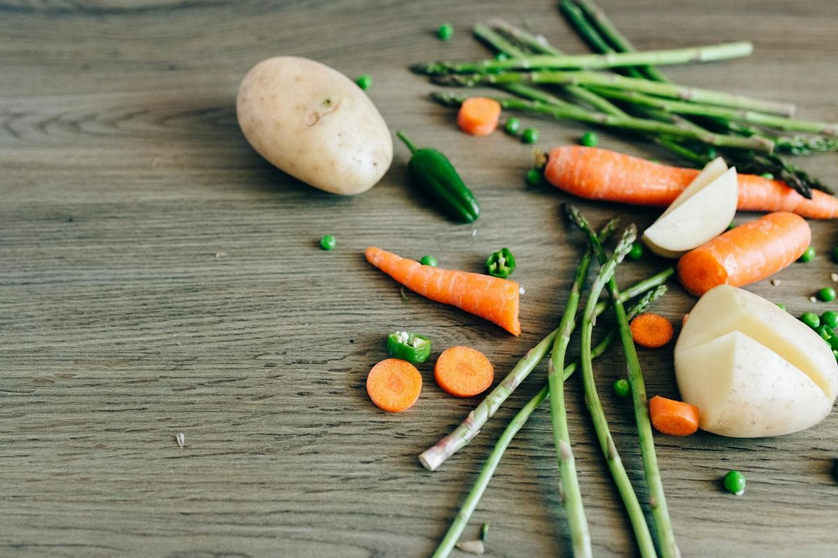 A variety of fresh organic vegetables — carrots, peas, asparagus — laid out on a wooden surface.