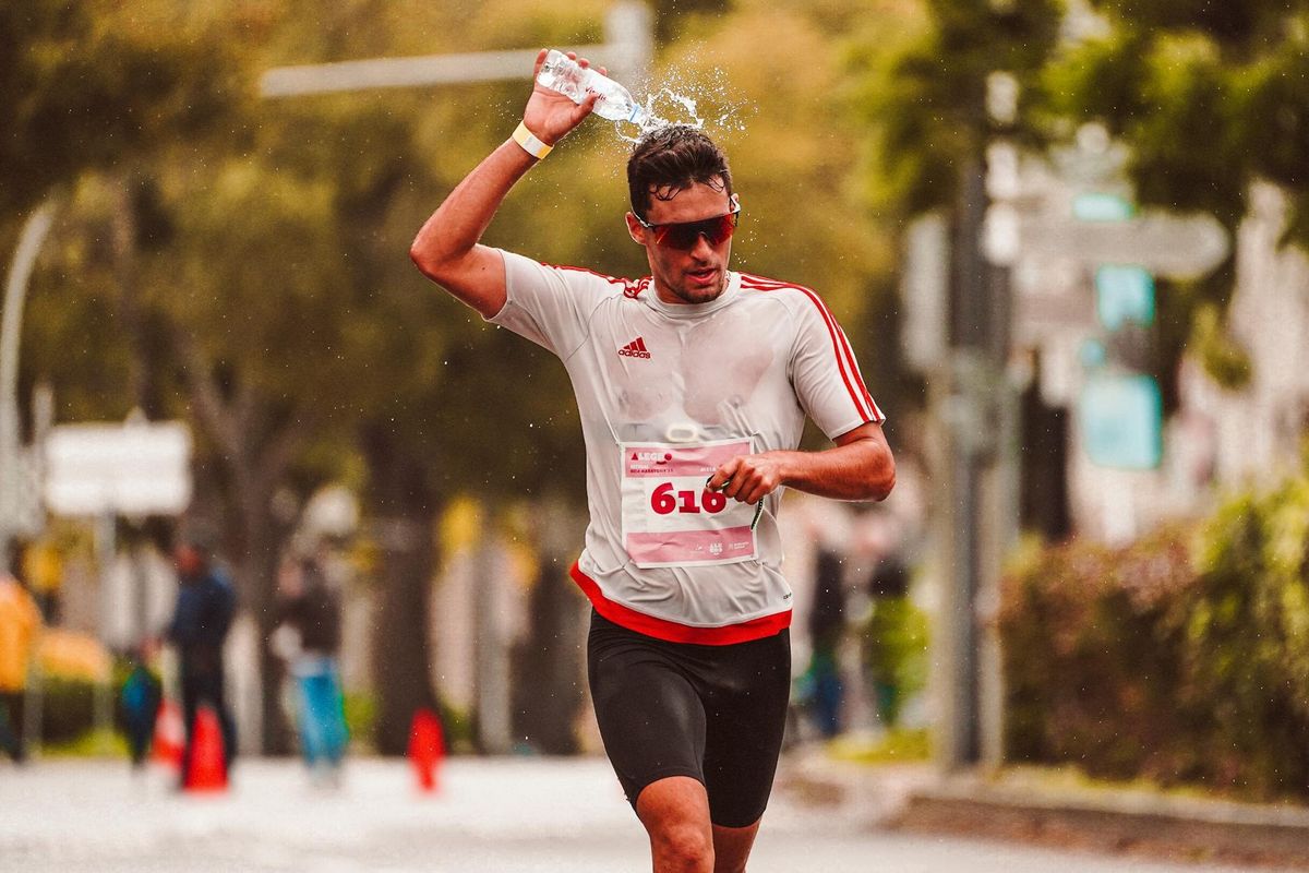 A marathon athlete pouring water over his head to cool down during an intense run.