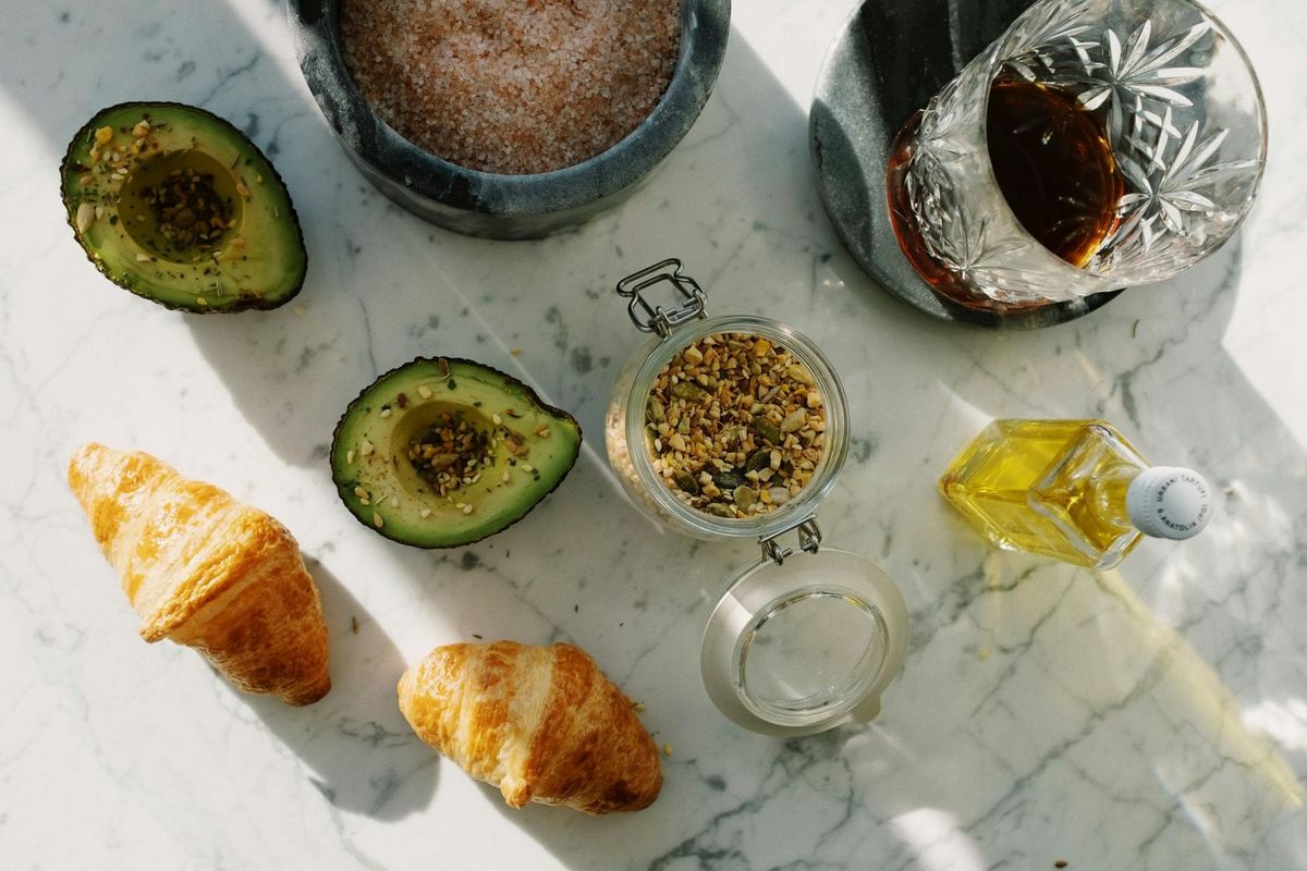 A nutritious breakfast setup with avocado, croissants, and seeds on marble.