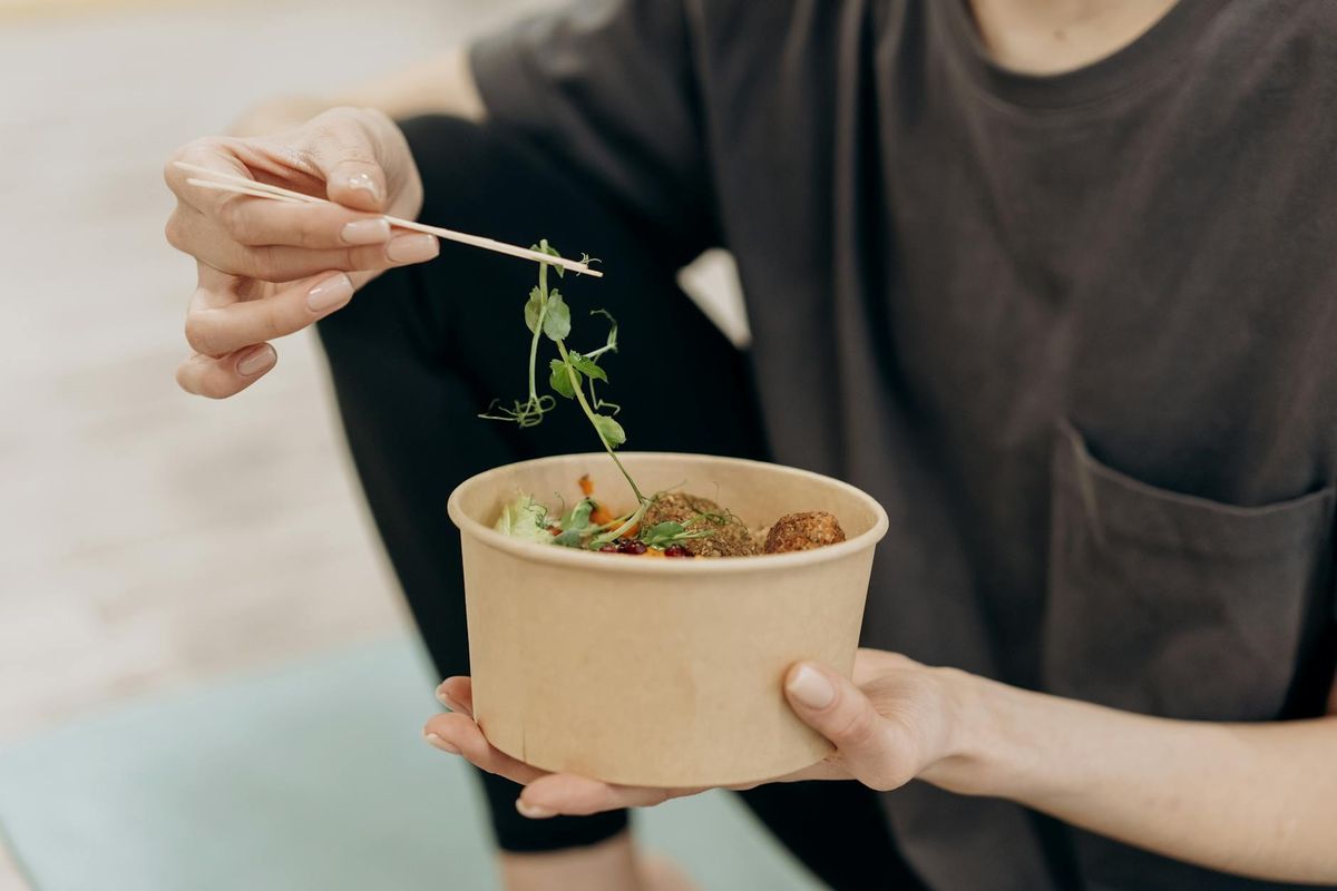 A woman holding a bowl filled with a healthy vegetarian meal in a calm indoor setting.